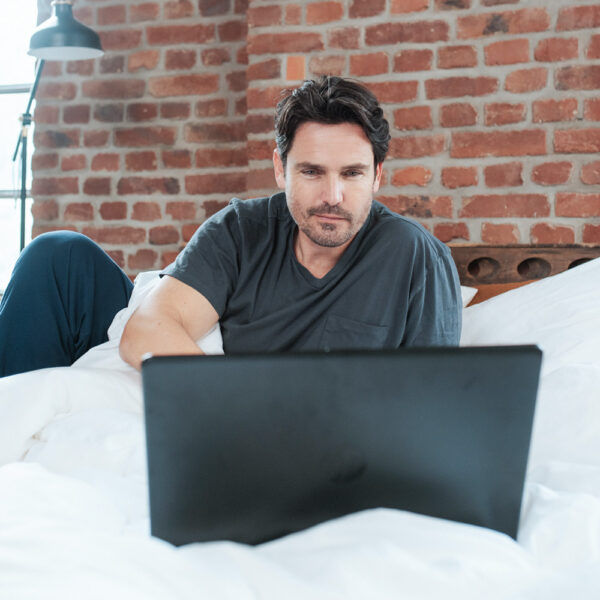 Mann nimmt Onlineberatung im Bett wahr