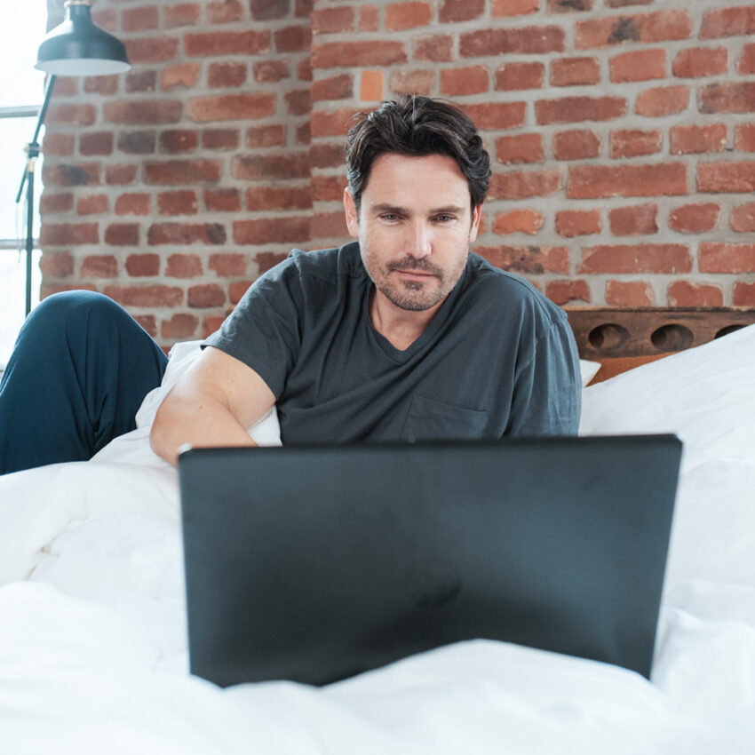 Mann nimmt Onlineberatung im Bett wahr
